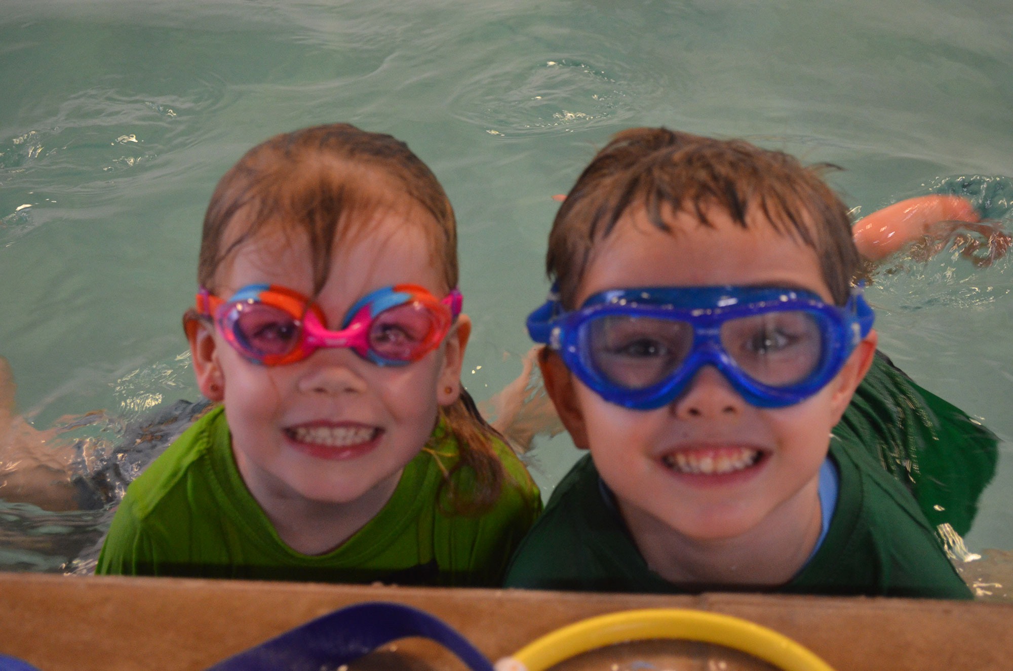 Two happy children in colourful goggles smiling in the pool